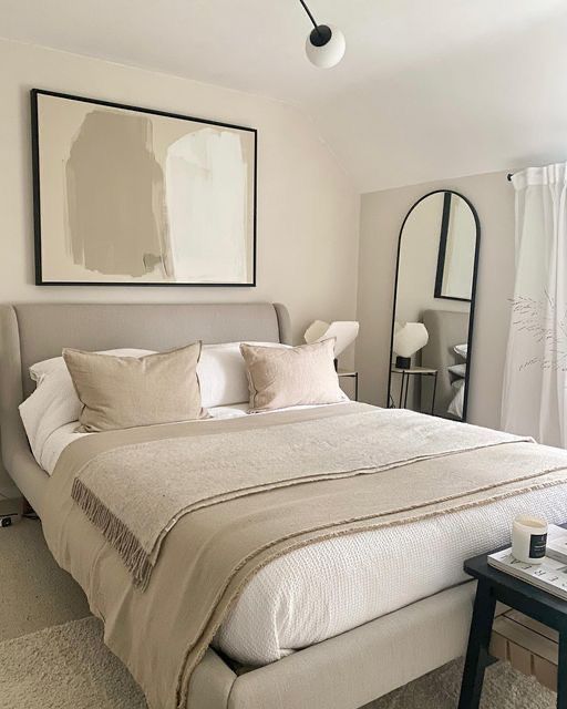 a bed with white sheets and pillows next to a table with a vase on it