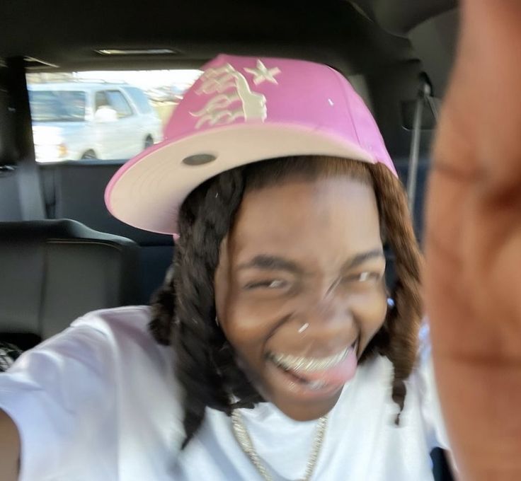 a young man wearing a pink hat and making a peace sign with his hand while sitting in the back seat of a car