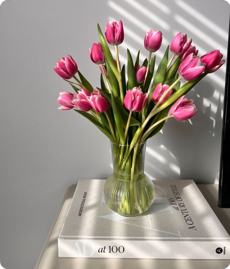 a vase filled with pink tulips on top of a book