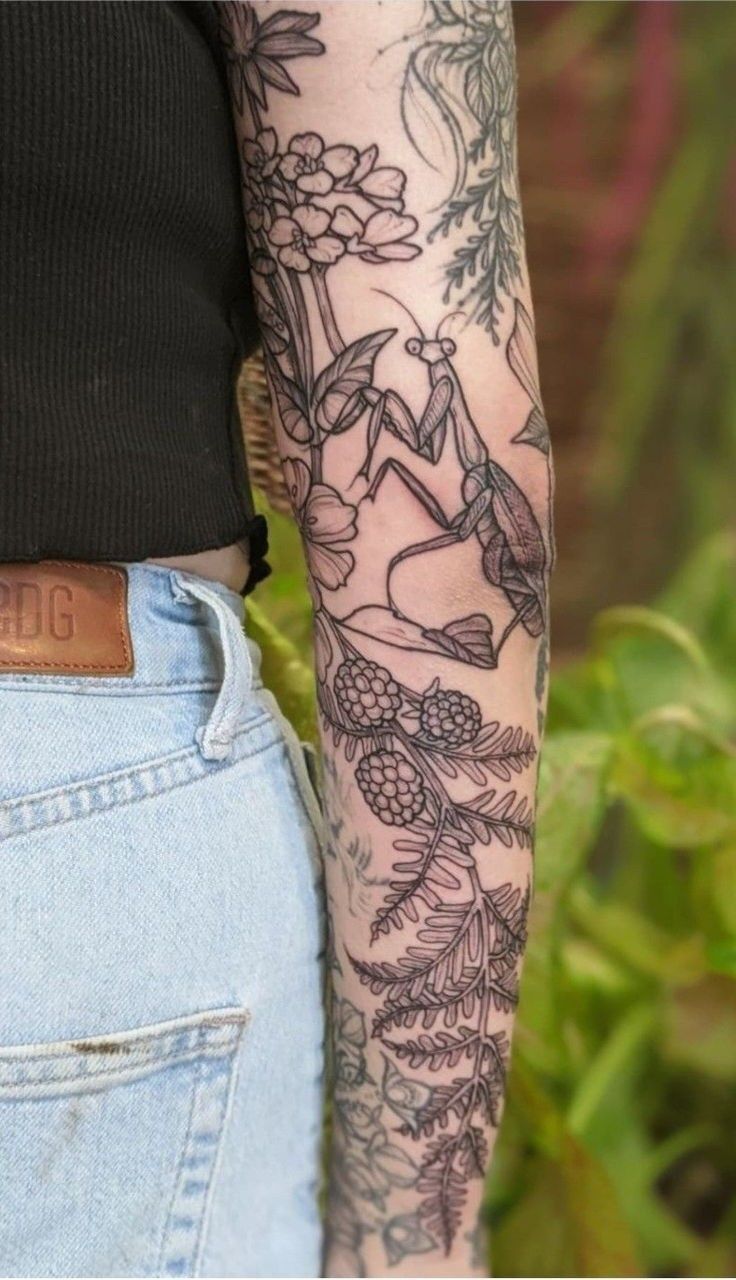 a woman with tattoos on her arm and leg is standing in front of some plants