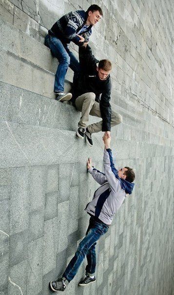 three young men climbing up the side of a wall