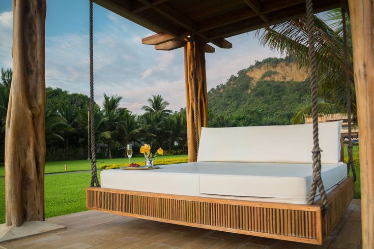 a white bed sitting on top of a wooden porch next to a lush green field