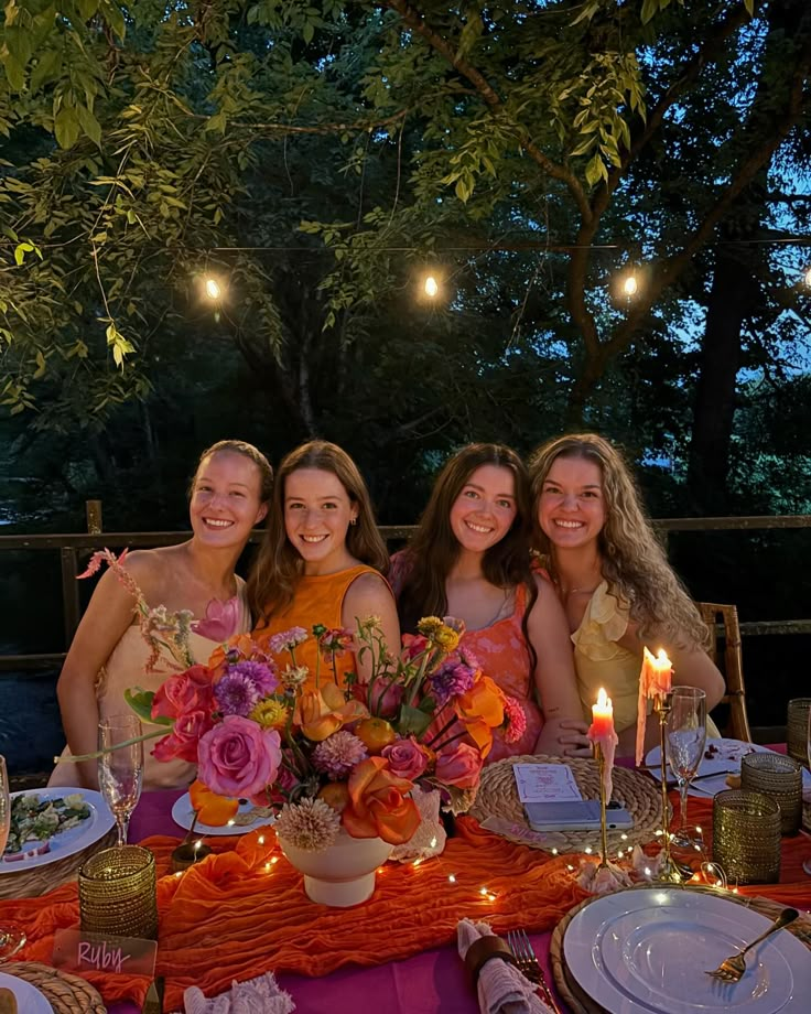 three women sitting at a table with plates and candles in front of them, posing for the camera