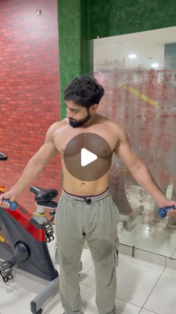 a man with no shirt on standing next to a stationary exercise bike in a gym