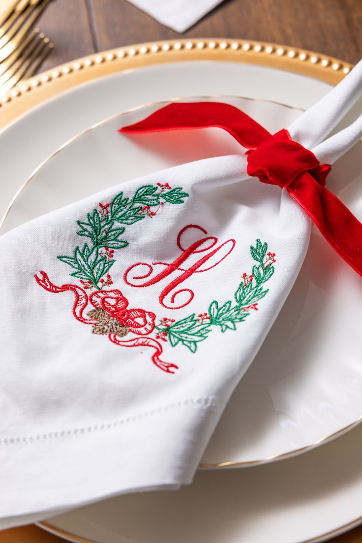 a white plate topped with a napkin covered in red ribbon and an embroidered monogram