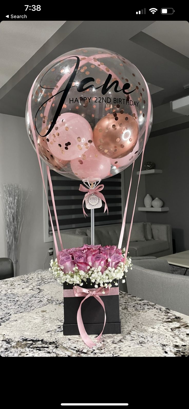 a balloon with some pink flowers in it on top of a table next to a black box