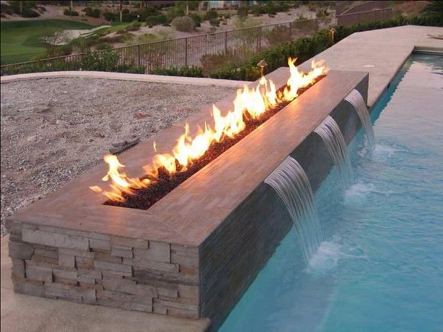 an outdoor fire pit in the middle of a swimming pool with water running from it