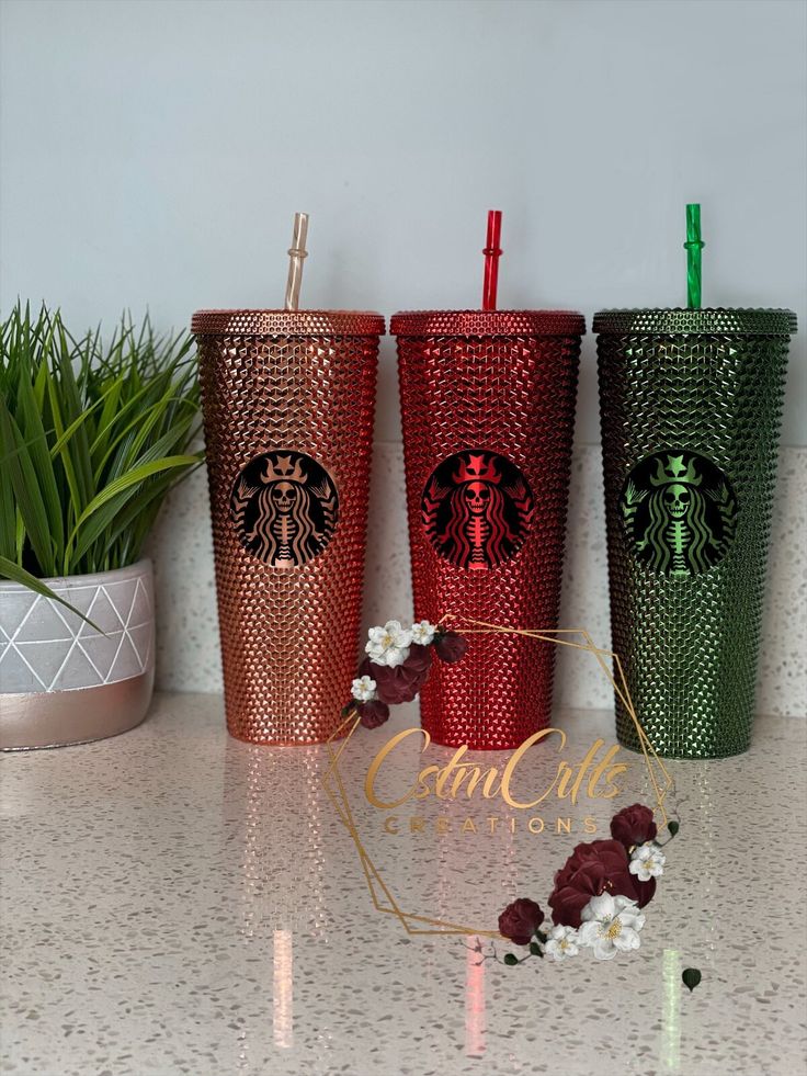 three starbucks cups sitting on top of a counter next to a potted green plant