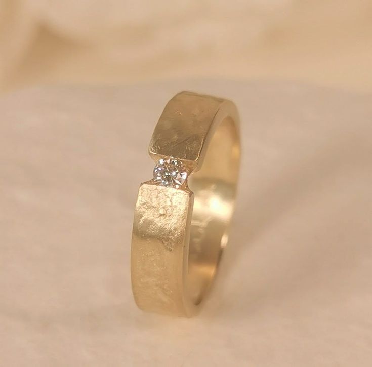 a yellow gold wedding ring with a single diamond on the top and bottom, sitting on a white sheet