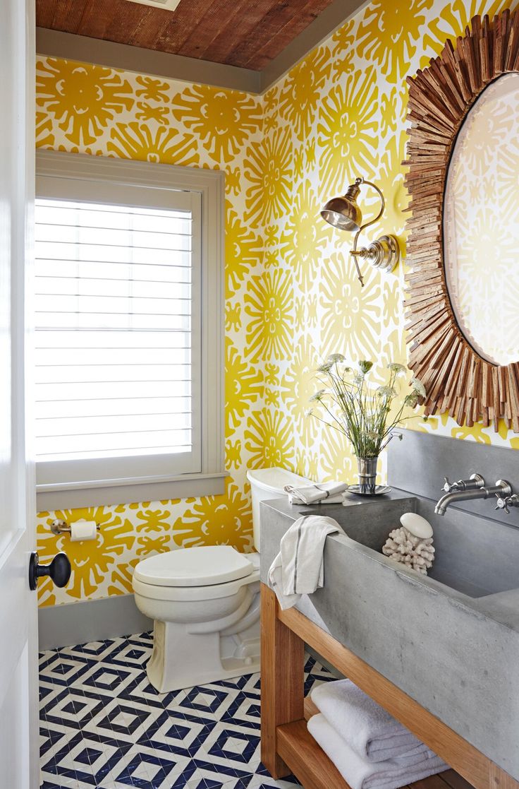 a bathroom decorated in yellow and white with a sink, mirror, toilet and window