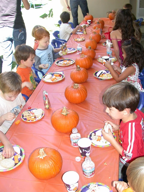 a group of children sitting at a table eating food with pumpkins in the background