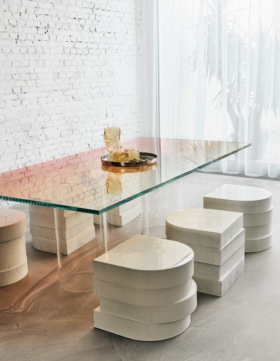 a glass table and four stools in front of a window with white brick walls