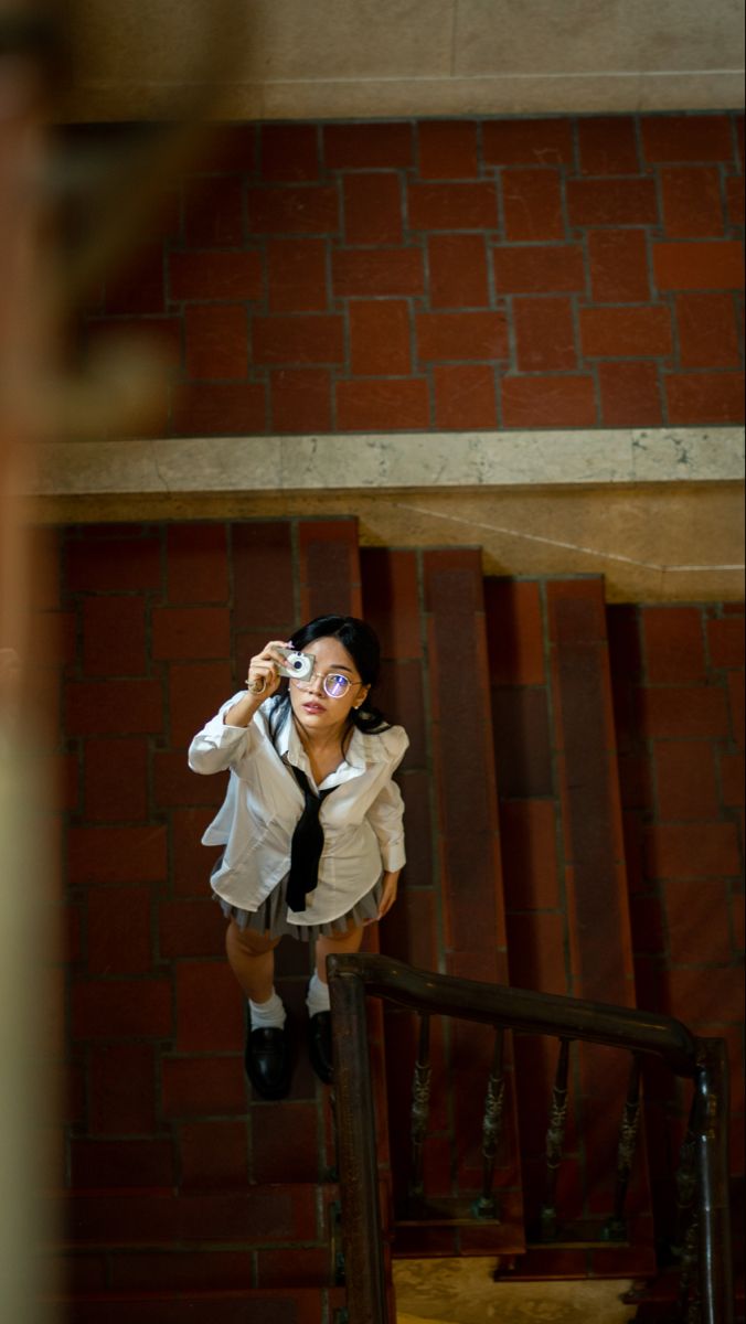 a woman in white shirt and tie standing on stairs with her hands behind her head