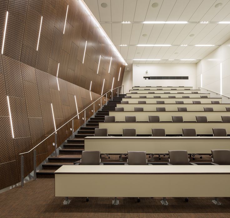 an empty lecture hall with rows of tables and chairs in front of a wall that has lights on it