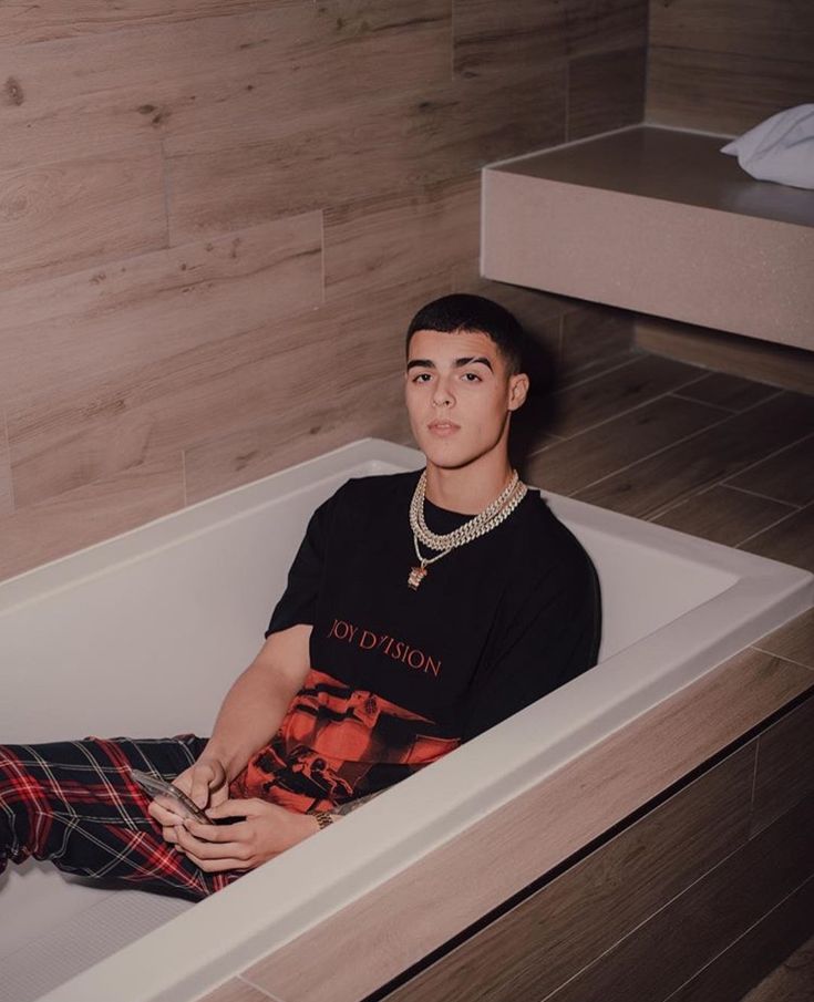 a young man sitting in a bathtub with his feet up on the edge of the tub