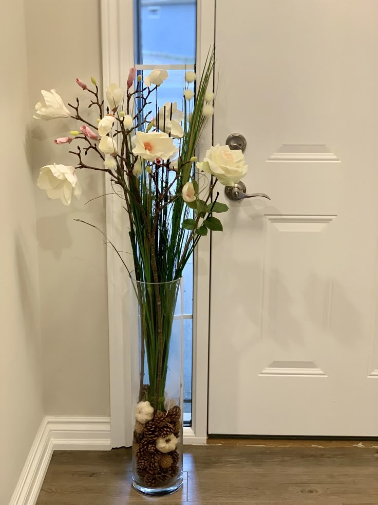 a vase filled with white flowers sitting on top of a wooden floor next to a door