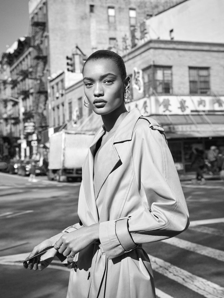 a black and white photo of a woman in a trench coat standing on the street