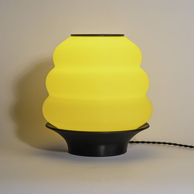 a yellow and black lamp on a white surface next to a brown cord that is plugged into the wall