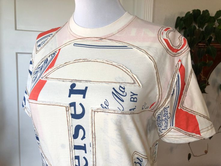 "Authentic Telfar Budweiser Customer T shirt. Soft cotton. Color is light cream/ivory with orange and blue print and brown top stitching. Double layered material with cutwork design. In excellent like new unworn condition. Shown on both men's mannequin with 36\" chest and women's mannequin with 34\" bust. Tag size XS (mens). Fits like womens S. shoulders seam to seam: sleeve: pit to pit: across waist: length:" Reworked Tshirt, Patchwork T Shirt, Mens Fits, Corporate Shirts, Fashion Design School, Custom Made T Shirts, Cream Shirt, Fashion Design Portfolio, Fashion Inspiration Design