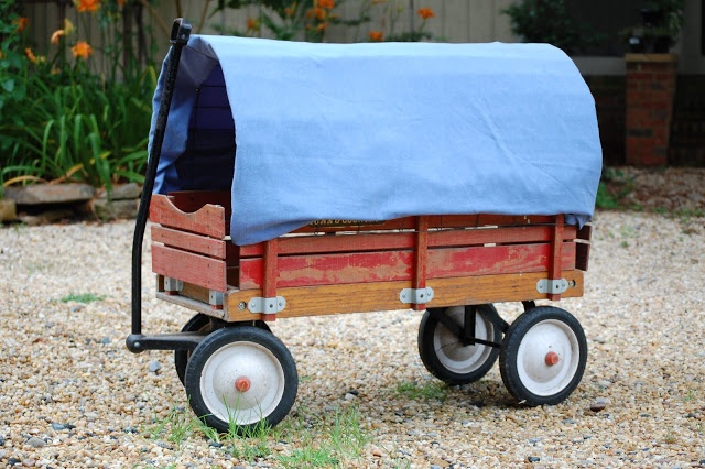 a wooden wagon with blue tarp on it's back and wheels, sitting in gravel