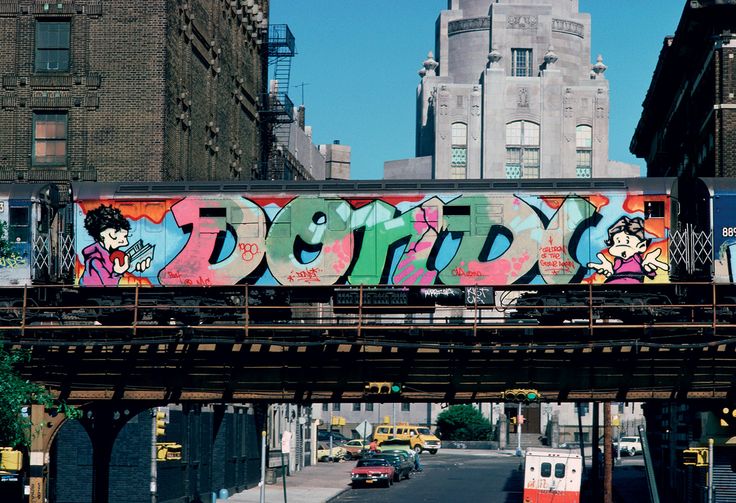 a train with graffiti on it is going over a bridge in the middle of an urban area