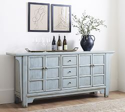 a blue buffet table with bottles and glasses on it in front of two framed pictures