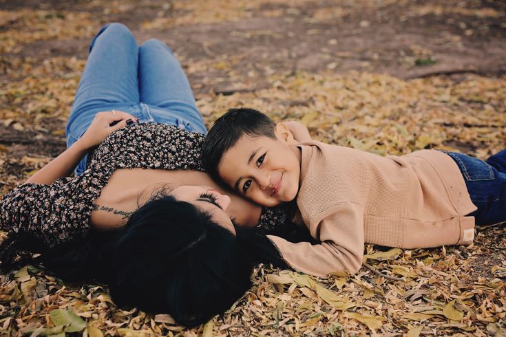 two people laying on the ground with leaves all around them and one person is smiling at the camera