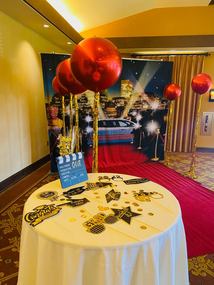 a white table topped with red and gold balloons in front of a large wall hanging from the ceiling