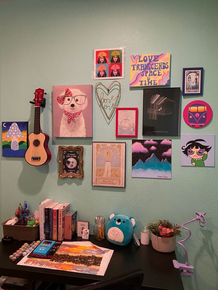 there are many pictures hanging on the wall next to a desk with a guitar and other items