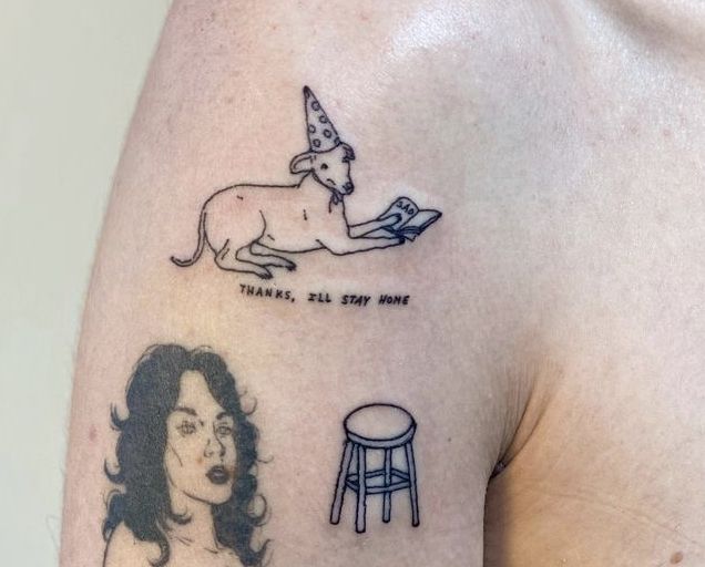 a woman's arm with tattoos on it and an image of a cat sitting on top of a stool