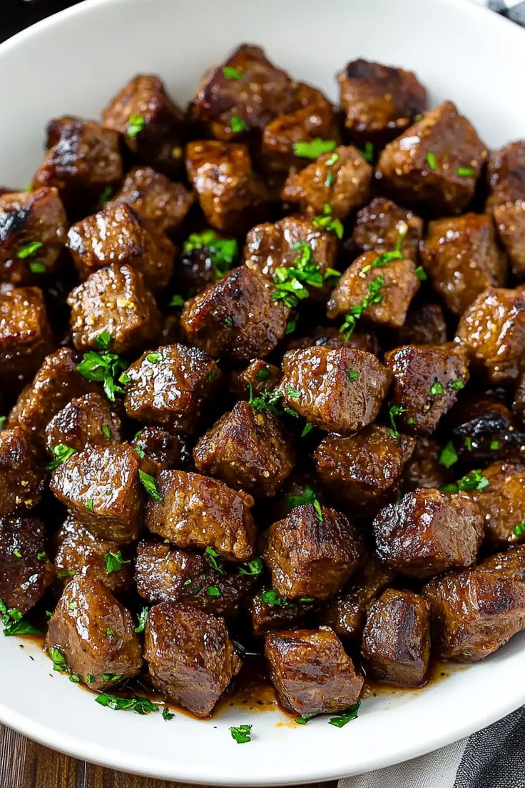 a white bowl filled with cooked meat and garnished with parsley on top