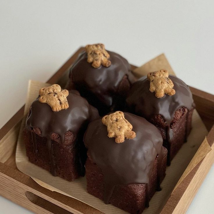 there are four brownies with chocolate frosting and cookies on top in a wooden tray