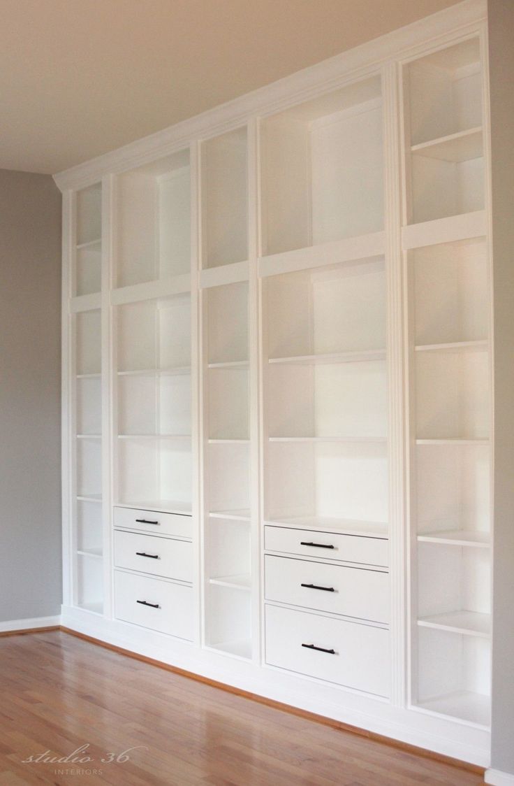 an empty room with white bookcases and hard wood floors