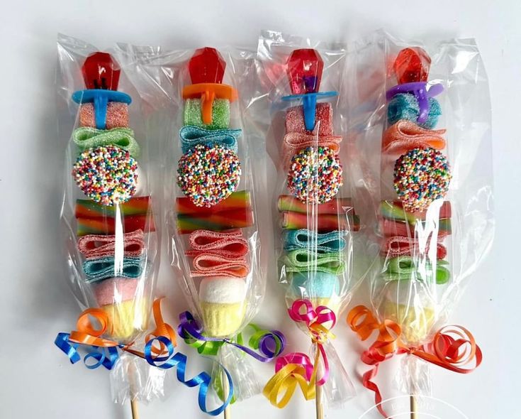 four lollipops wrapped in plastic with ribbons and bows on the top one is filled with sprinkles