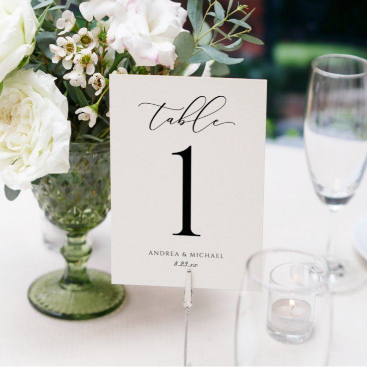 the table numbers are displayed in vases with white flowers and greenery on them