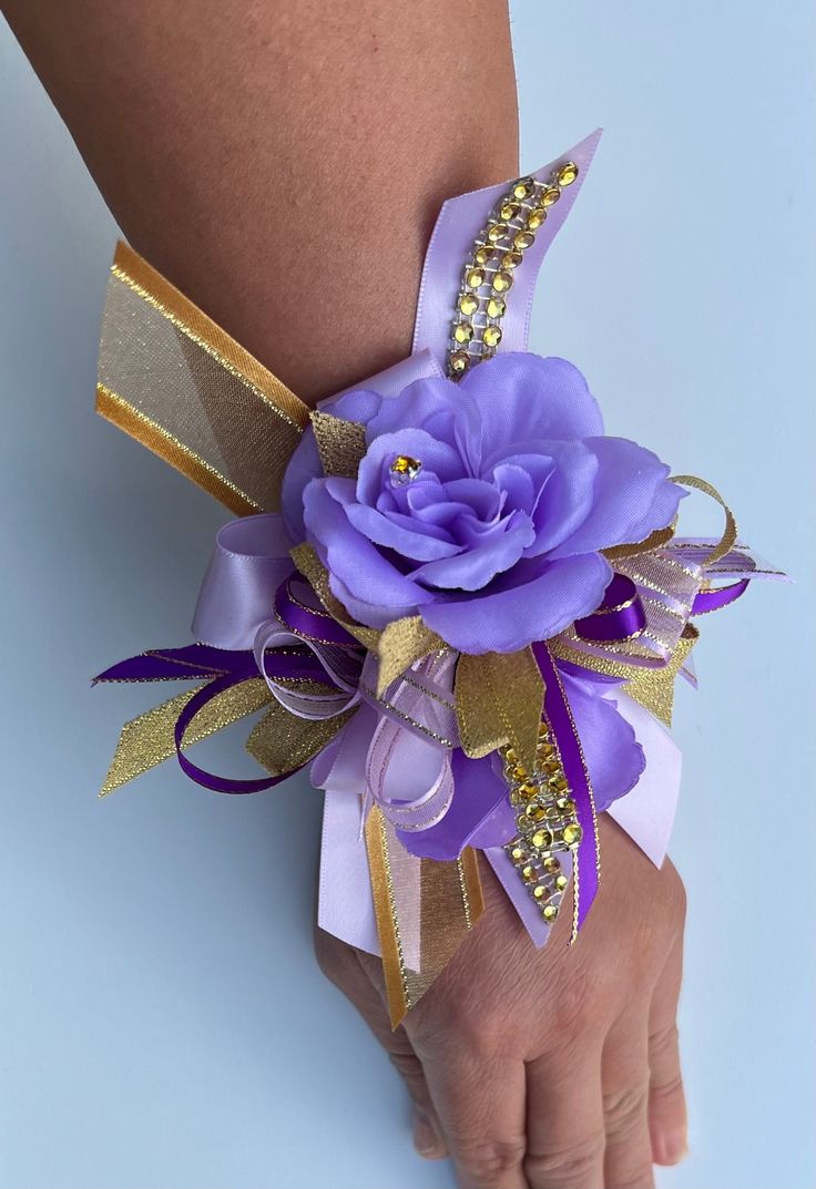 a purple and gold wrist corsage on someone's left hand, with a flower in the center