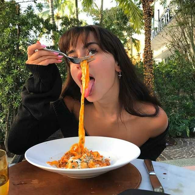 a woman eating spaghetti with her mouth open and holding a fork in front of her face