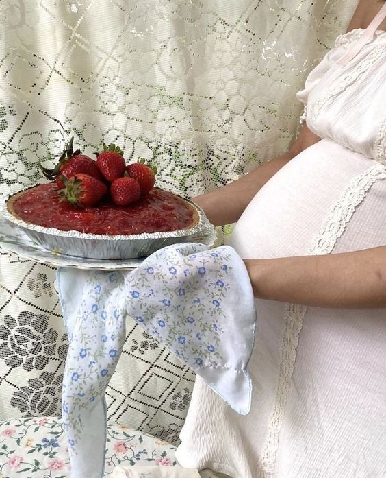 a pregnant woman holding a plate with strawberries on it