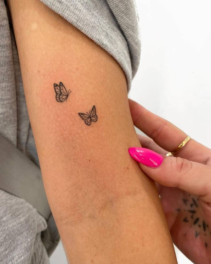 a woman's arm with two small butterflies on the back of her left arm