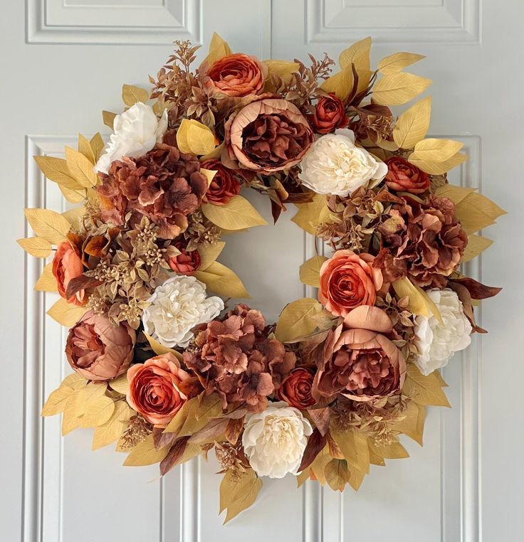 a wreath is hanging on the front door with flowers and leaves around it in fall colors