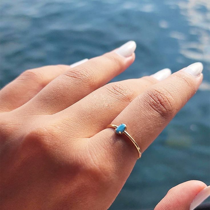 a woman's hand holding a cell phone and wearing a gold ring with a turquoise stone