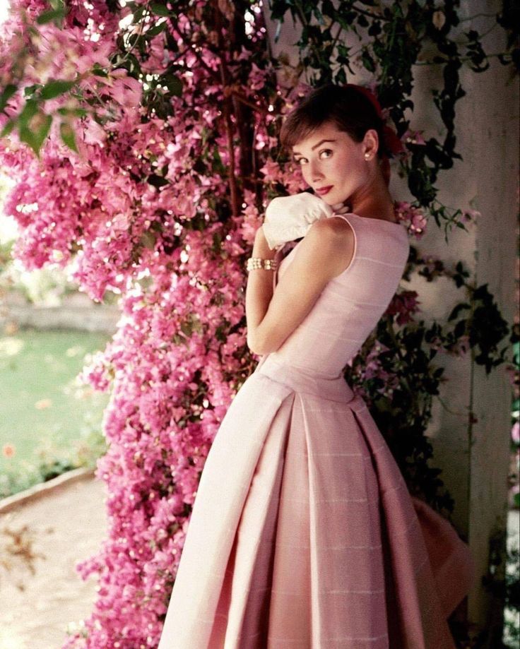 a woman in a pink dress standing next to flowers