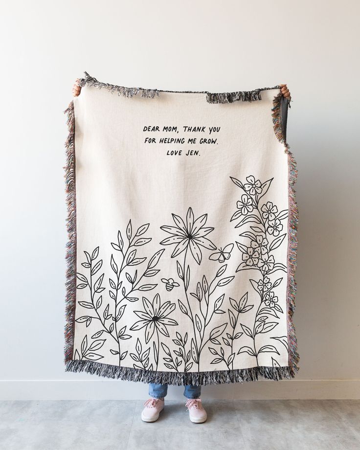 a woman standing in front of a wall holding up a blanket with flowers on it