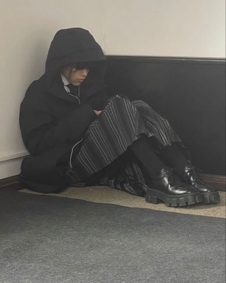 a person sitting on the floor in front of a wall with their legs crossed and wearing black boots