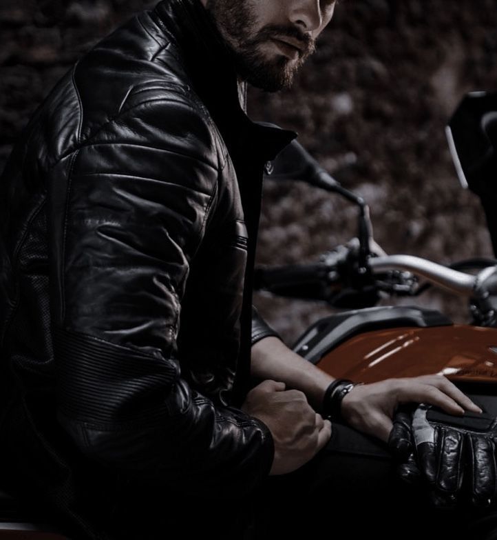 a man sitting on a motorcycle with his hand on the handlebars and wearing a leather jacket