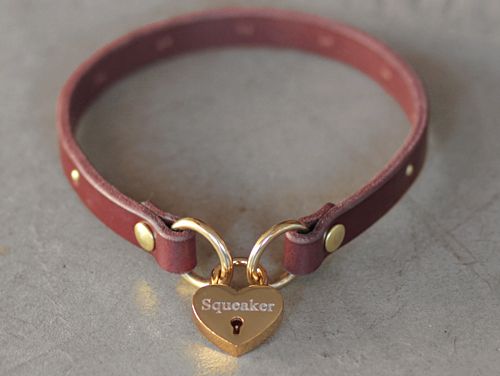 a red leather collar with a heart shaped lock on the front, and a name tag attached to it