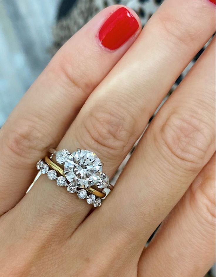 a woman's hand with a red manicured nail polish and two engagement rings