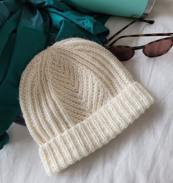 a white hat and sunglasses on top of a bed next to some folded up clothing