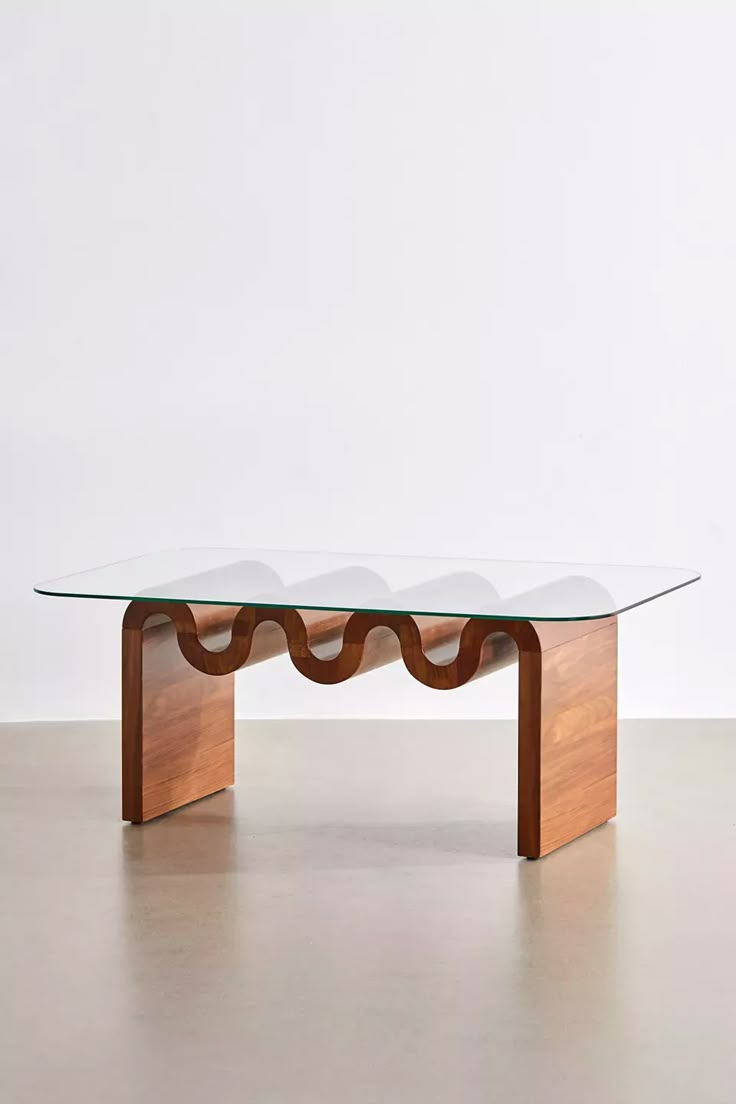 a glass and wood coffee table with wavy curves on the top, in front of a white wall