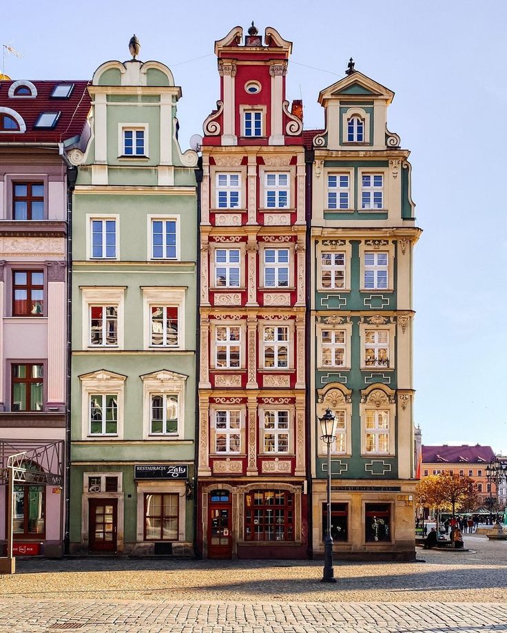 many different colored buildings are in the middle of a cobblestone street with a clock tower on top